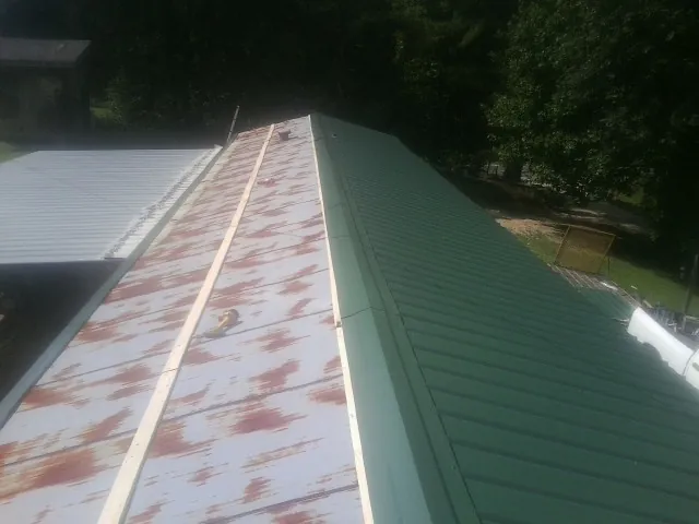 Old rusted panels beside newly installed green metal roofing — Wind Damage Roof Repair by Roofing Brothers in Warsaw